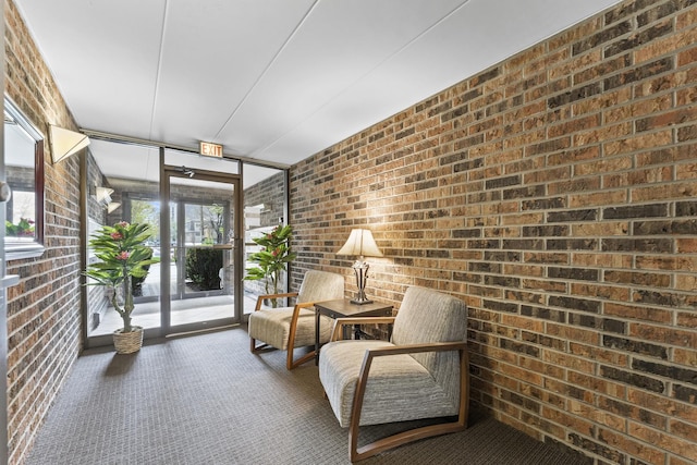 sitting room featuring carpet flooring, floor to ceiling windows, and brick wall