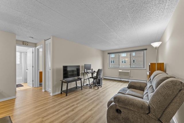 living room with a textured ceiling, light wood-type flooring, baseboards, a baseboard radiator, and an AC wall unit