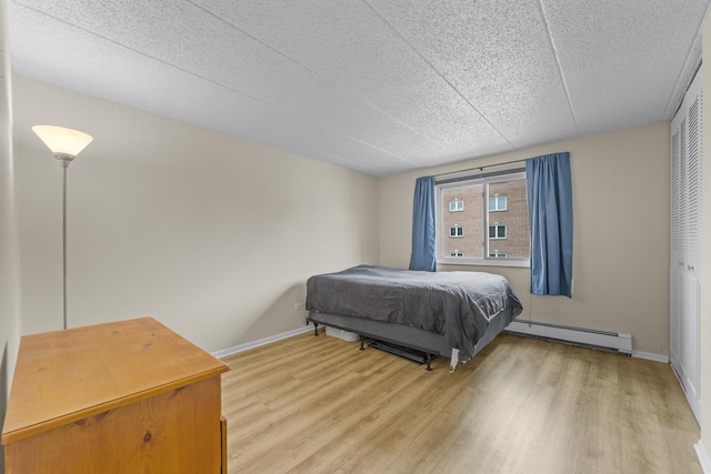bedroom with light wood-type flooring, a textured ceiling, baseboards, and baseboard heating