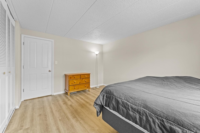 bedroom with baseboards, a closet, light wood-type flooring, and a textured ceiling