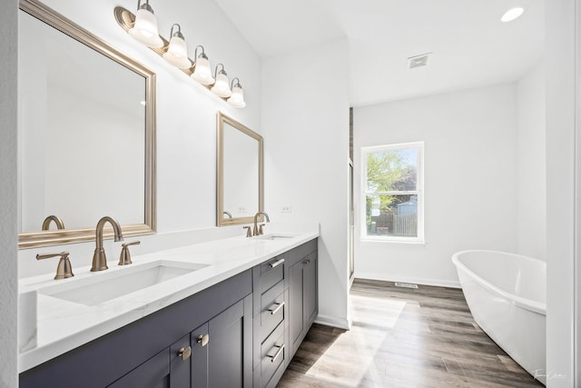 bathroom with double vanity, a soaking tub, wood finished floors, and baseboards