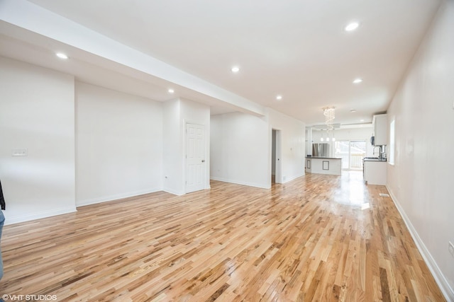 unfurnished living room featuring an inviting chandelier, recessed lighting, baseboards, and light wood-style floors