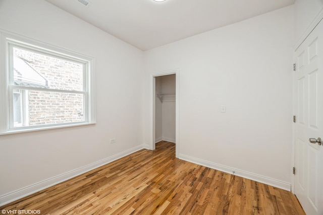 unfurnished bedroom with light wood finished floors, a walk in closet, baseboards, and a closet