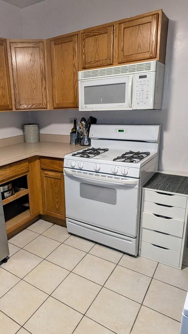kitchen with white appliances, brown cabinetry, light tile patterned floors, and light countertops