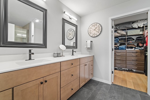 bathroom featuring double vanity, baseboards, a walk in closet, and a sink