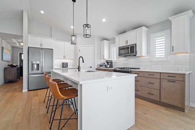 kitchen with appliances with stainless steel finishes, a breakfast bar, a sink, tasteful backsplash, and an island with sink
