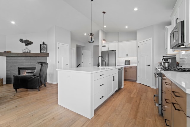 kitchen with stainless steel appliances, a kitchen island with sink, light countertops, decorative backsplash, and vaulted ceiling