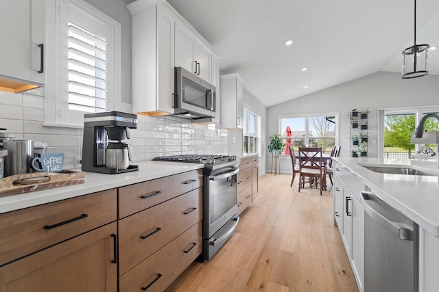 kitchen featuring a sink, lofted ceiling, light wood-type flooring, light countertops, and appliances with stainless steel finishes