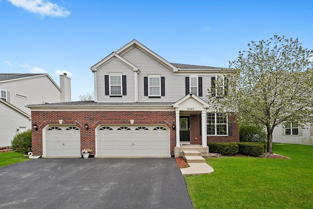 traditional home with brick siding, driveway, a front yard, and roof with shingles