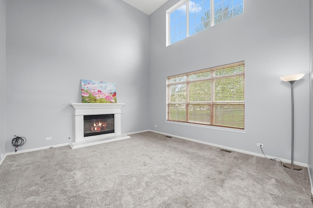 unfurnished living room with a high ceiling, visible vents, a glass covered fireplace, and carpet floors