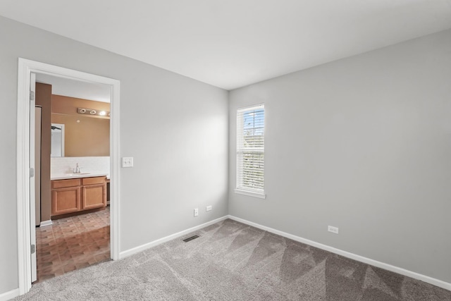 unfurnished bedroom with baseboards, light colored carpet, visible vents, and a sink
