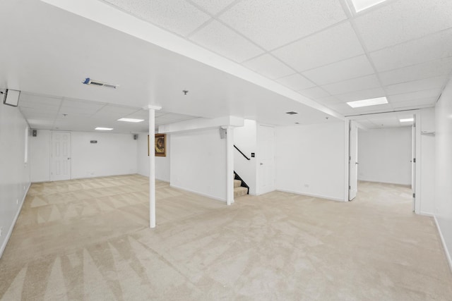 finished below grade area featuring a paneled ceiling, light carpet, and stairway