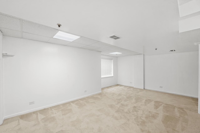 empty room featuring a paneled ceiling, light colored carpet, baseboards, and visible vents