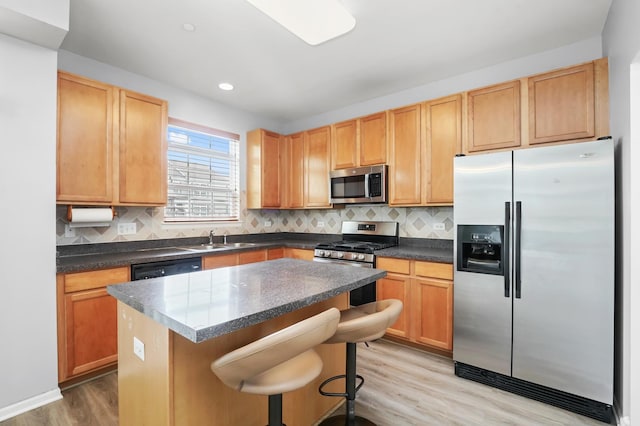 kitchen featuring light wood-style flooring, a sink, backsplash, dark countertops, and appliances with stainless steel finishes