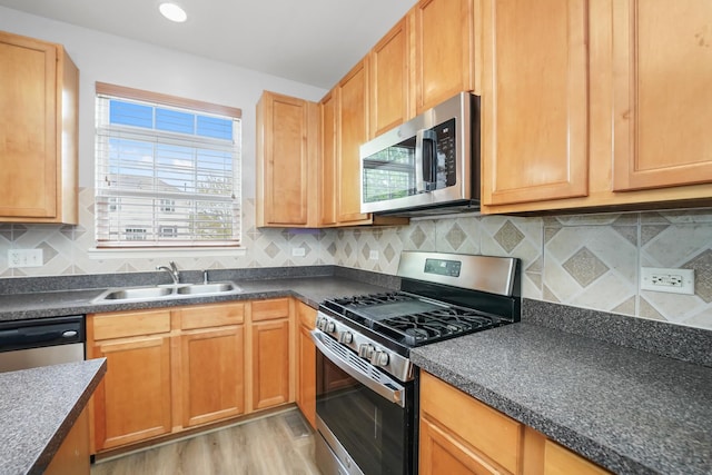 kitchen featuring a sink, stainless steel appliances, tasteful backsplash, light wood-type flooring, and dark countertops
