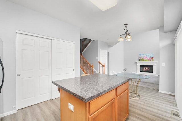 kitchen with light wood-type flooring, visible vents, a center island, dark countertops, and a glass covered fireplace