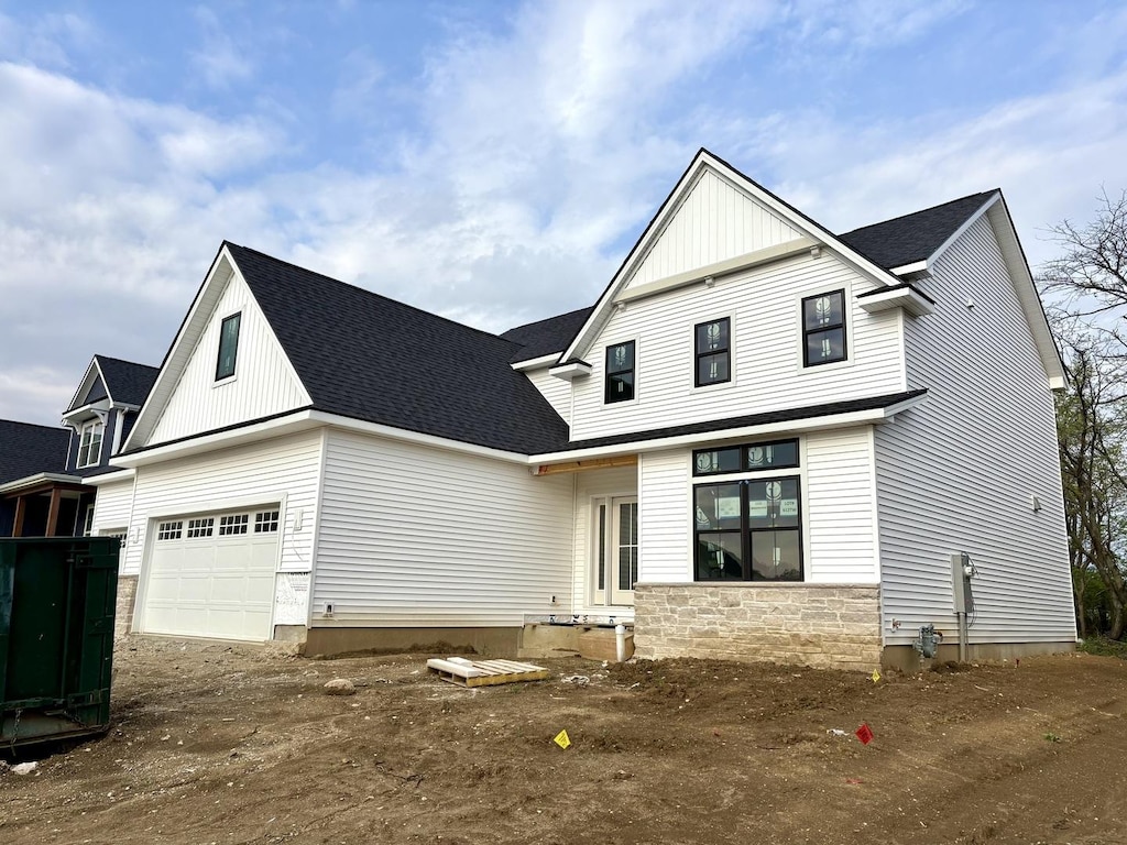 view of front facade with board and batten siding, dirt driveway, a shingled roof, and stone siding