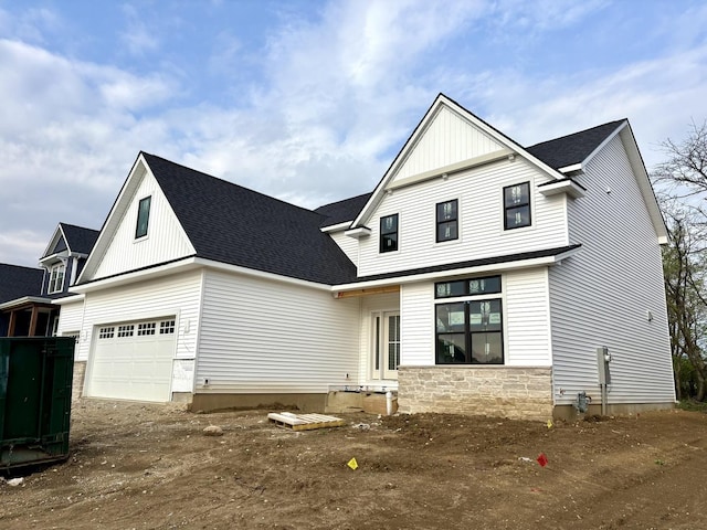 view of front facade with board and batten siding, dirt driveway, a shingled roof, and stone siding
