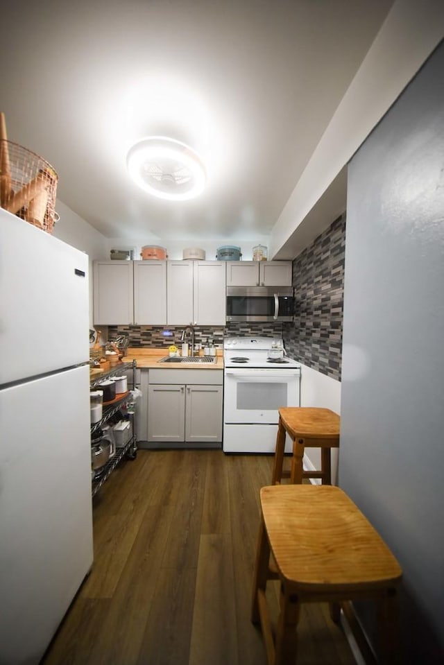 kitchen featuring a sink, white appliances, light countertops, dark wood finished floors, and decorative backsplash