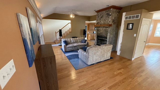 living area with ceiling fan, a stone fireplace, visible vents, stairway, and light wood finished floors