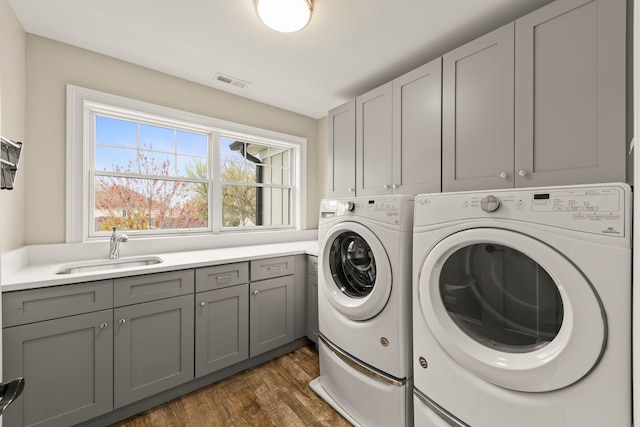washroom featuring visible vents, dark wood-style floors, washing machine and clothes dryer, a sink, and cabinet space