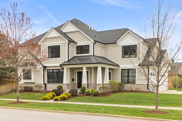 view of front of house with a shingled roof, a front lawn, stone siding, a porch, and a standing seam roof