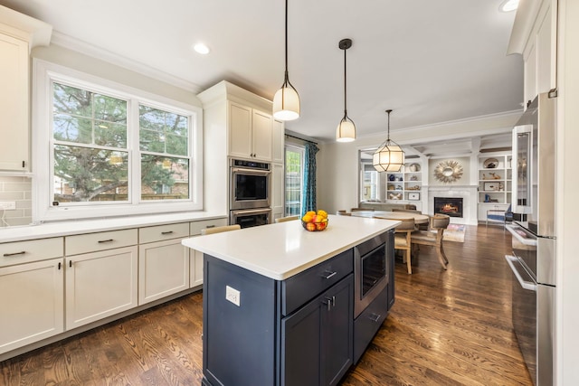 kitchen with appliances with stainless steel finishes, light countertops, open floor plan, dark wood-type flooring, and ornamental molding