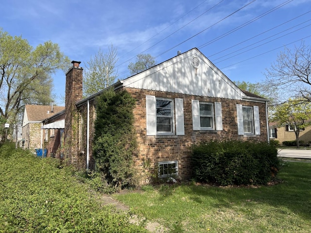 view of property exterior with brick siding, a yard, and a chimney