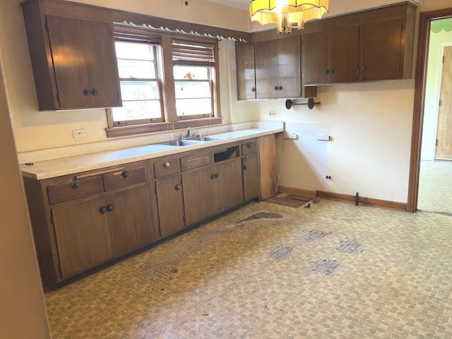 kitchen with light countertops, dark brown cabinets, baseboards, and a sink