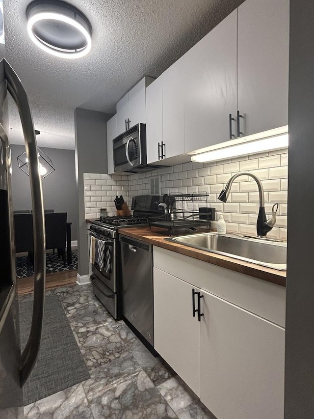 1216 S New Wilke Rd Unit 106, Arlington Heights, IL 60005 - kitchen featuring a textured ceiling, white cabinets, a sink, backsplash, and stainless steel appliances