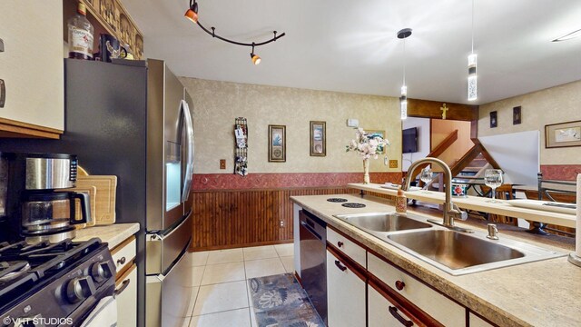 kitchen with wainscoting, a sink, light countertops, light tile patterned floors, and dishwashing machine
