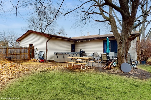 back of property with fence, a hot tub, a lawn, and a patio