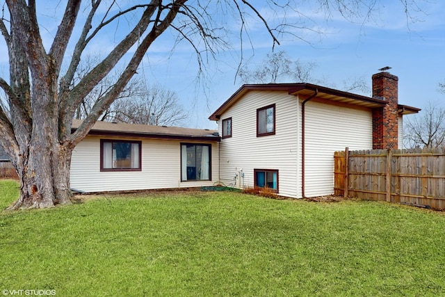 rear view of property with fence, a yard, and a chimney