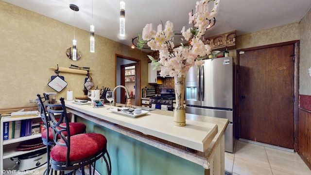 kitchen featuring a peninsula, light tile patterned flooring, a sink, appliances with stainless steel finishes, and hanging light fixtures