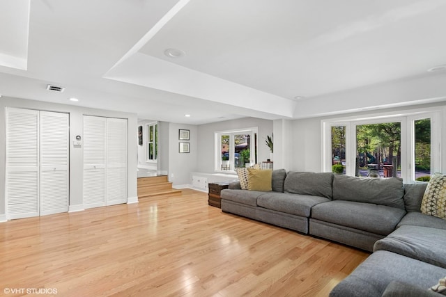 living room with healthy amount of natural light, a raised ceiling, light wood-style flooring, and recessed lighting