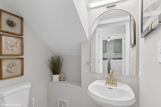half bath featuring a sink, washing machine and dryer, toilet, and vaulted ceiling