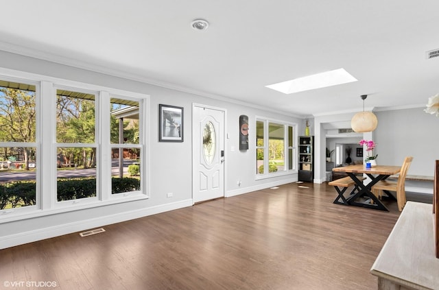 entrance foyer with a skylight, ornamental molding, plenty of natural light, baseboards, and wood finished floors