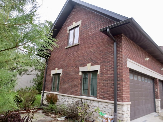 view of side of home with an attached garage, brick siding, stone siding, and concrete driveway
