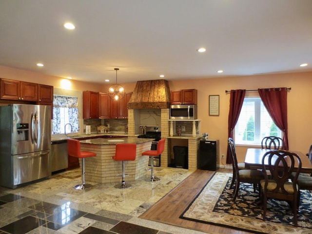 kitchen featuring a kitchen breakfast bar, appliances with stainless steel finishes, a center island, custom range hood, and recessed lighting