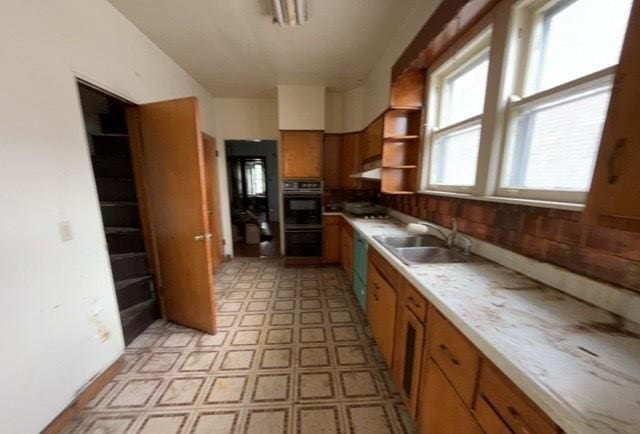 kitchen featuring open shelves, a sink, light countertops, brown cabinetry, and light floors