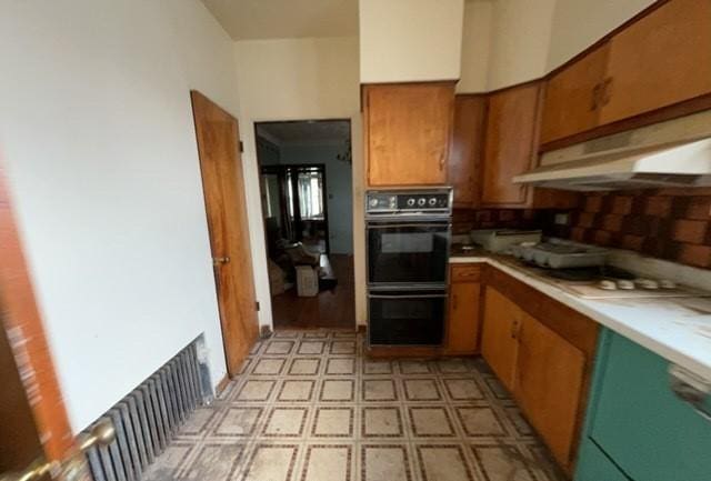 kitchen featuring brown cabinets, light countertops, dobule oven black, light floors, and under cabinet range hood