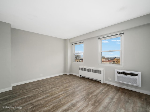 spare room featuring an AC wall unit, baseboards, wood finished floors, and radiator
