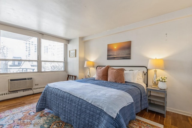 bedroom featuring wood finished floors, baseboard heating, an AC wall unit, and baseboards