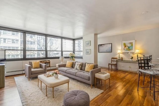 living area with a baseboard heating unit, healthy amount of natural light, and wood finished floors