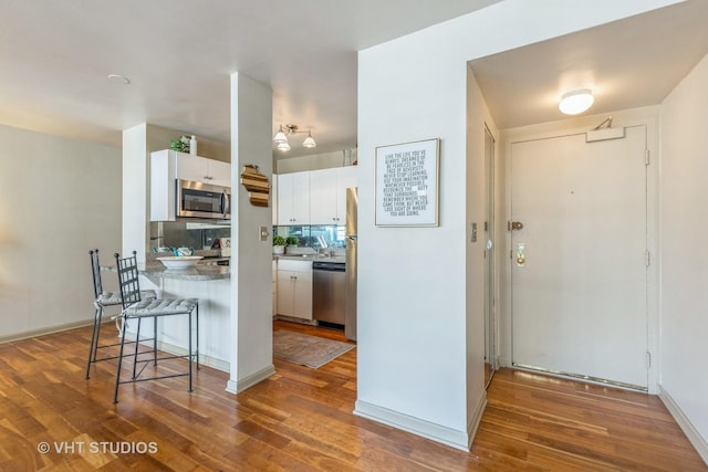 kitchen featuring stainless steel appliances, a peninsula, a kitchen breakfast bar, white cabinets, and wood finished floors