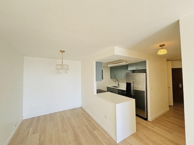 kitchen with stainless steel refrigerator with ice dispenser, a sink, light wood-style flooring, light countertops, and baseboards