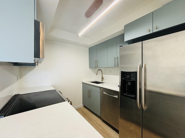 kitchen featuring appliances with stainless steel finishes, a sink, light wood finished floors, light countertops, and baseboards