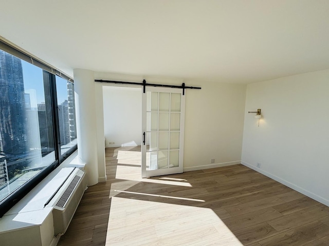 unfurnished bedroom with a barn door, wood finished floors, baseboards, and a wall mounted air conditioner