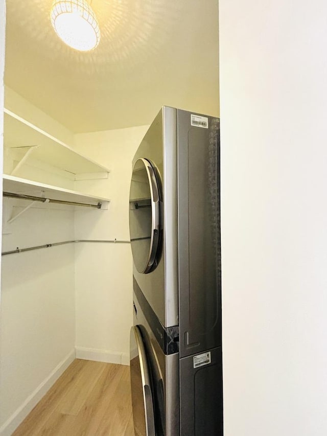 clothes washing area with stacked washer / dryer, light wood-style floors, and baseboards