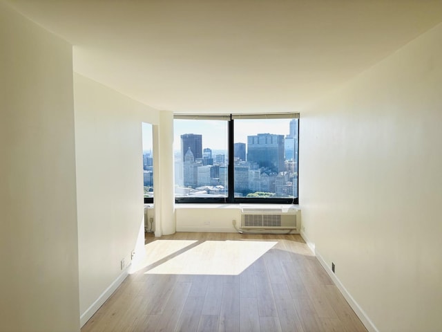 spare room featuring a wall unit AC, wood finished floors, a city view, and baseboards